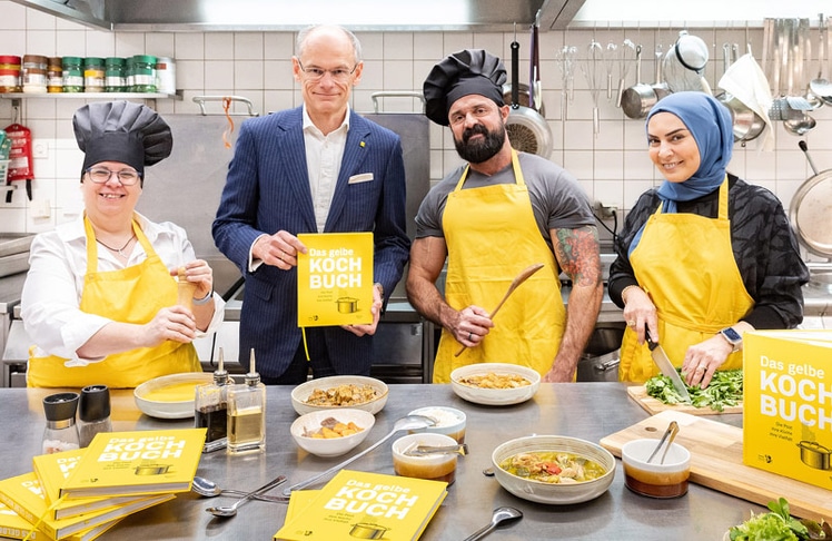 "Das gelbe Kochbuch" mit Rezepten von  Barbara Zissler, Douglas de Oliveira Batista, Gülseren Gülmez (v.l.n.r.) und 77 weiteren Mitarbeiter:innen der Post. Hier gemeinsam mit Walter Oblin, Generaldirektor Österreichische Post AG (2.v.l.)